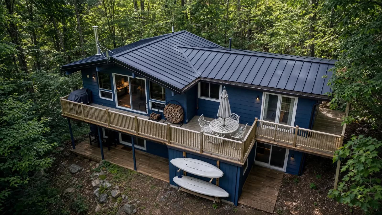 Dark standing seam roof on a blue cottage surrounded by woodland