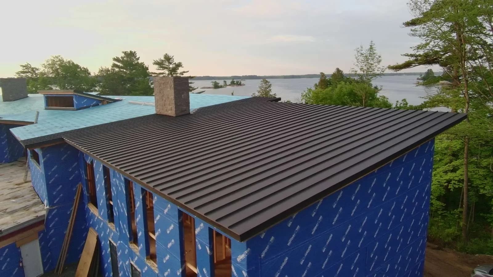Standing seam roof above a lakeside building wrapped in blue membrane