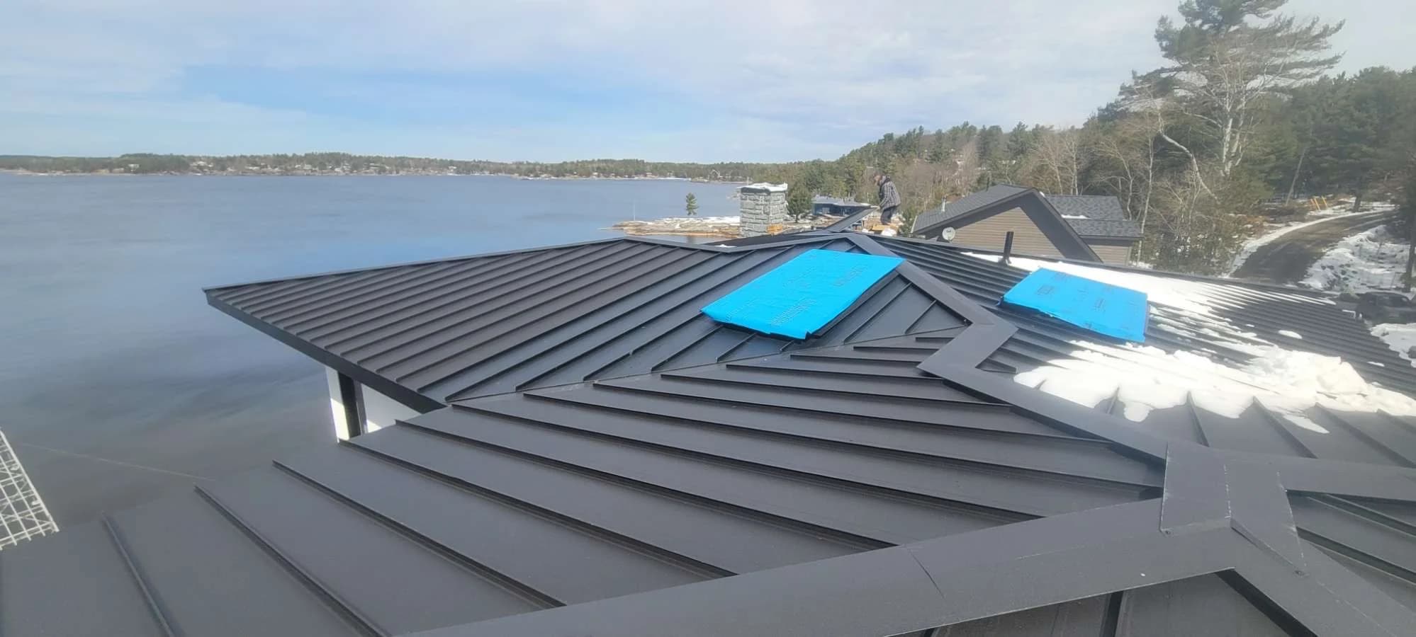 Dark metal roof hips overlooking the water during installation