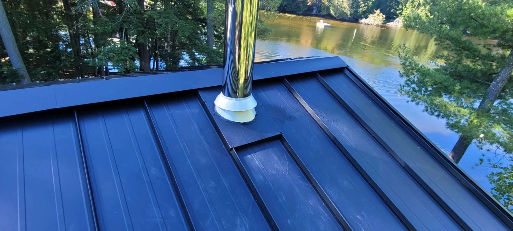 Dark metal roof around a chimney flue beside the water