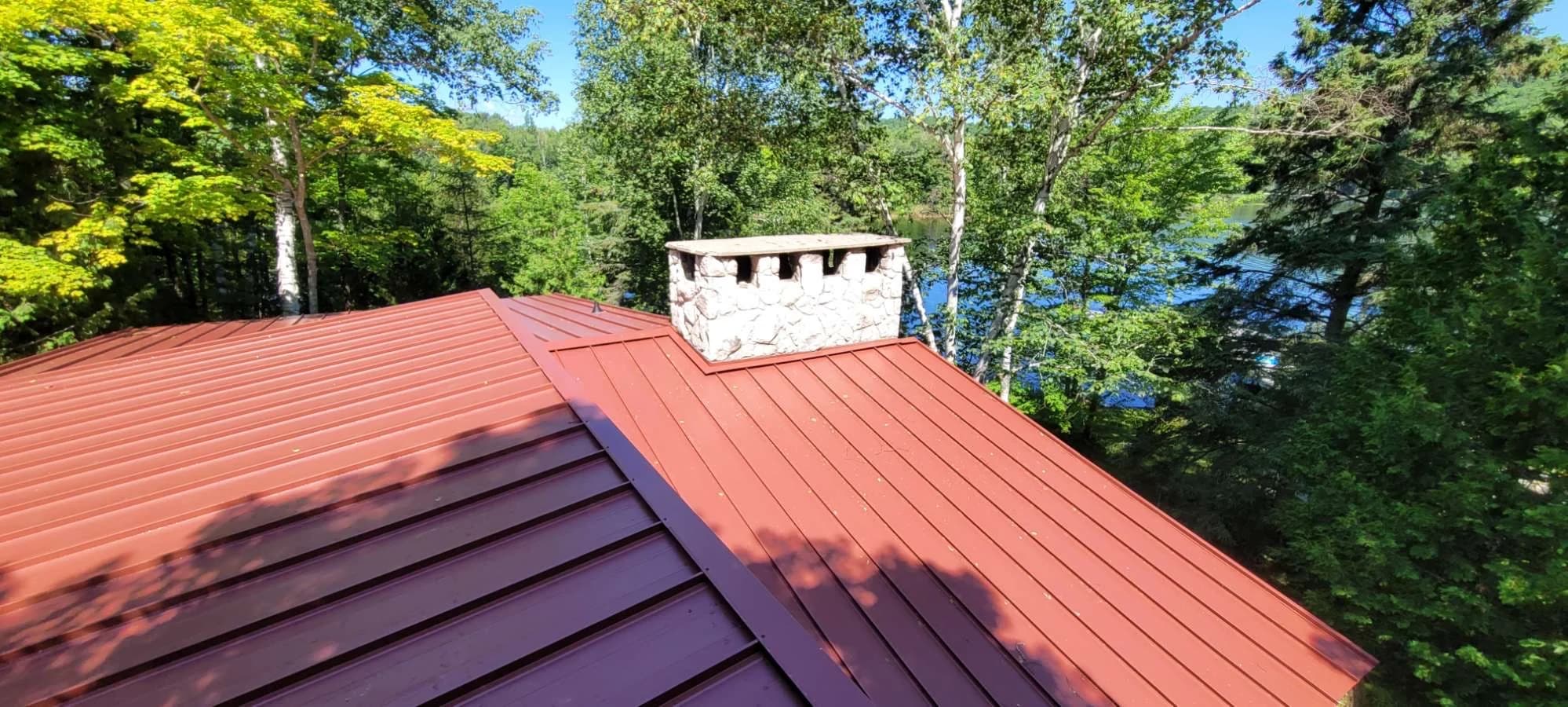Red standing seam roof and chimney beside woodland