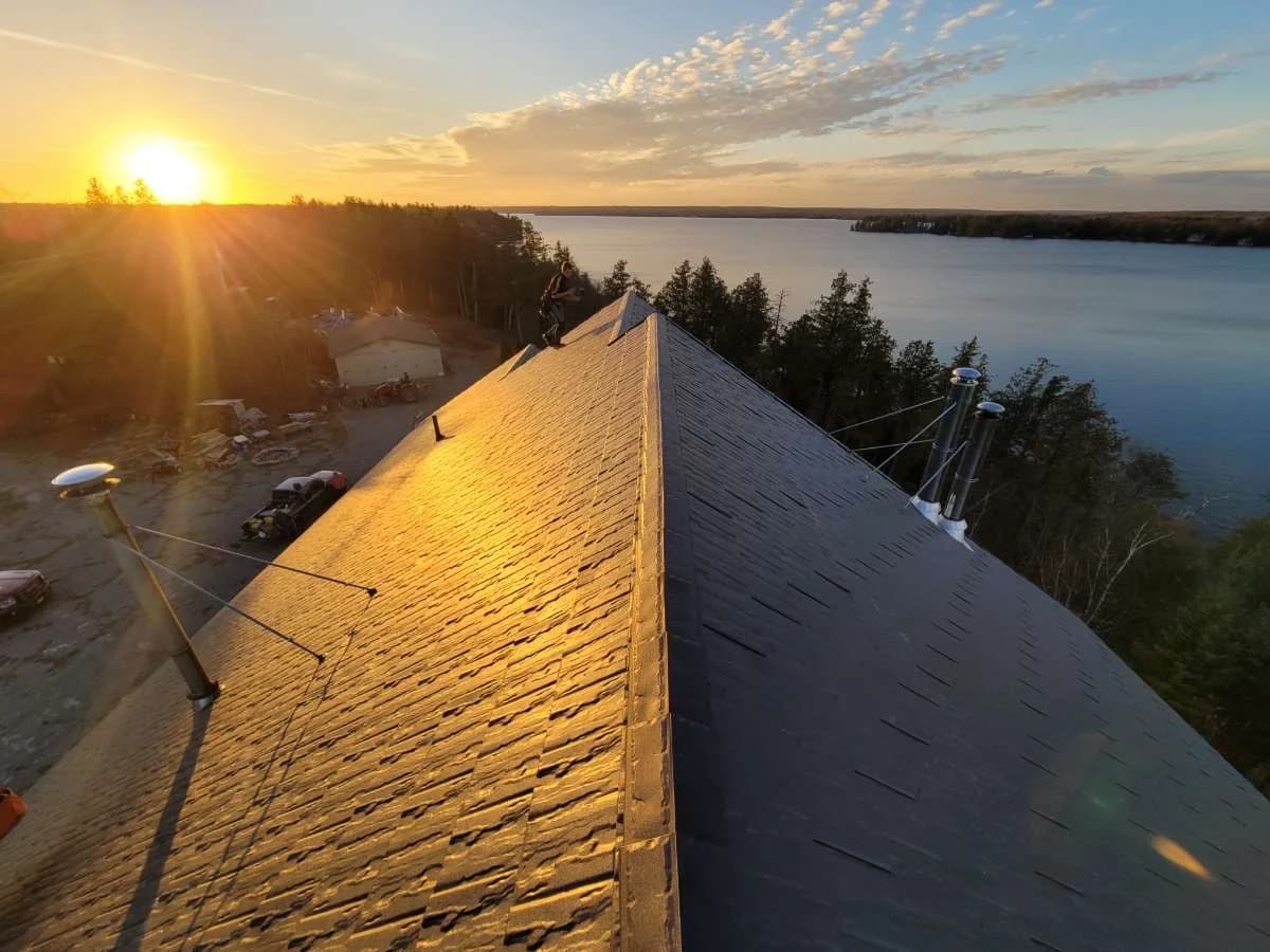 Sunset reflecting along a metal shingle roof ridge beside the water