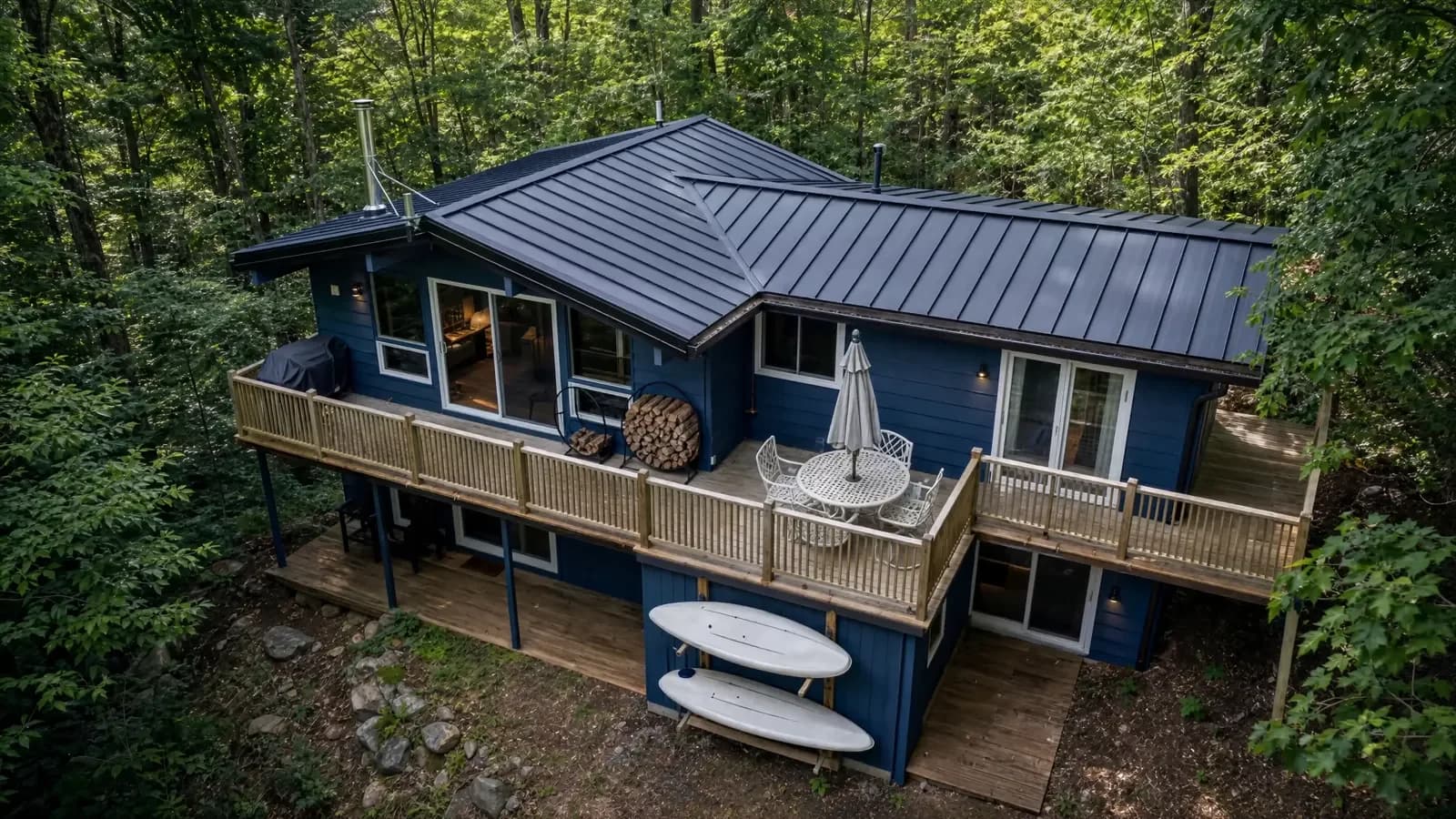 Completed standing seam roof on a blue cottage surrounded by woodland